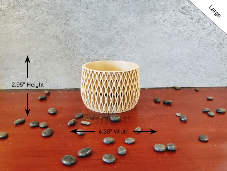 May include: A light brown wooden planter with a diamond pattern design. The planter is 4.35 inches wide and 2.95 inches high. The planter is sitting on a red wooden surface with black stones scattered around it.
