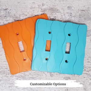 May include: Two light switch covers, one orange and one blue, with a wavy design. The covers are made of a textured material and have a modern look.
