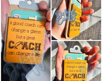 May include: A wooden clipboard with a yellow note attached. The note reads "a good coach can change a game but a great COACH can change a life". The note has a football graphic on it.