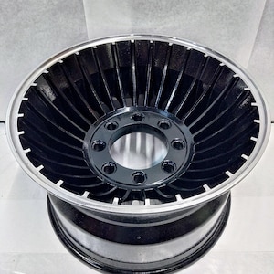 Puede incluir: Rueda negra y plateada con un dise&ntilde;o de turbina. La rueda tiene una llanta plateada y un centro negro con una serie de radios que irradian hacia afuera.