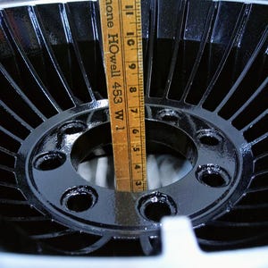 Puede incluir: Una rueda de metal negro con un cubo central y cinco agujeros para tornillos. La rueda tiene un dise&ntilde;o de radios radiales y tiene un di&aacute;metro de aproximadamente 30 cm.