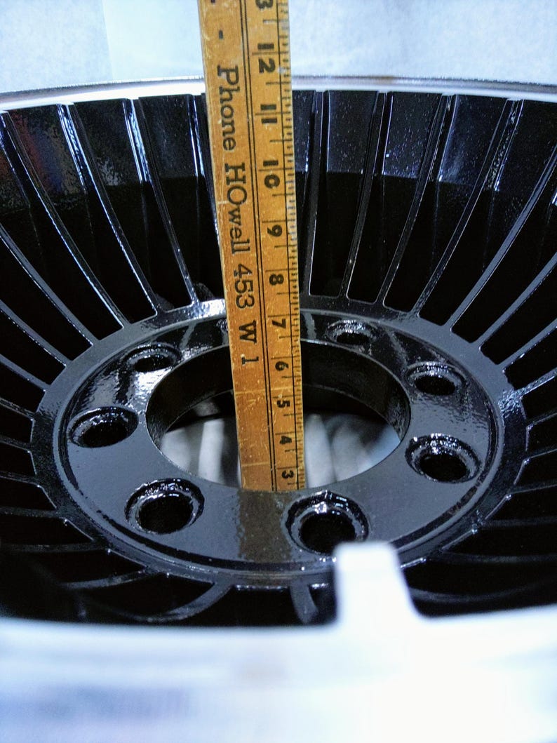 Puede incluir: Una rueda de metal negro con un cubo central y cinco agujeros para tornillos. La rueda tiene un dise&ntilde;o de radios radiales y tiene un di&aacute;metro de aproximadamente 30 cm.