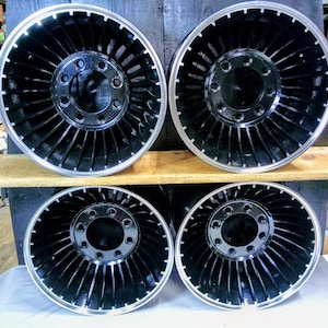 Puede incluir: Cuatro ruedas negras de estilo turbina con un borde plateado. Las ruedas tienen una tapa central negra con varios agujeros.