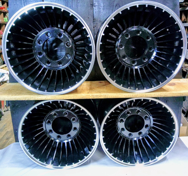 Puede incluir: Cuatro ruedas negras de estilo turbina con un borde plateado. Las ruedas tienen una tapa central negra con varios agujeros.