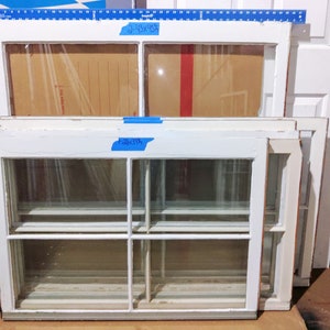 Puede incluir: Cuatro marcos de ventanas de madera blanca apilados uno encima del otro. El marco superior tiene una etiqueta que dice "2-43x43". El segundo marco tiene una etiqueta que dice "26x39".