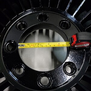 Puede incluir: Una rueda de metal negro con una abertura circular en el centro. La abertura se mide con una cinta m&eacute;trica amarilla, mostrando un di&aacute;metro de 12,7 cm. La rueda tiene una serie de radios que irradian desde el centro.