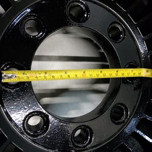 Puede incluir: Primer plano de una rueda de metal negro con un di&aacute;metro de 17 pulgadas, medida con una cinta m&eacute;trica amarilla.