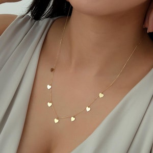 May include: A gold necklace with a delicate chain and multiple small heart charms hanging from it.