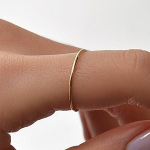 Könnte beinhalten: Ein schlichter goldener Ring, der an einem Finger mit hellrosa Nagellack getragen wird.