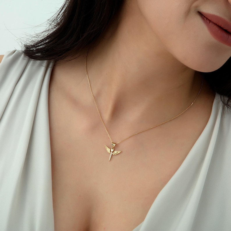 May include: A gold chain necklace with a small angel pendant. The angel has wings and a body with a small diamond-like detail.