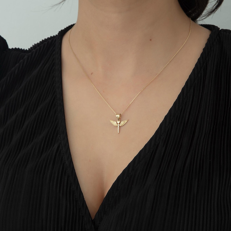May include: A gold necklace with a pendant featuring a heart with wings. The pendant is detailed with small sparkling stones.