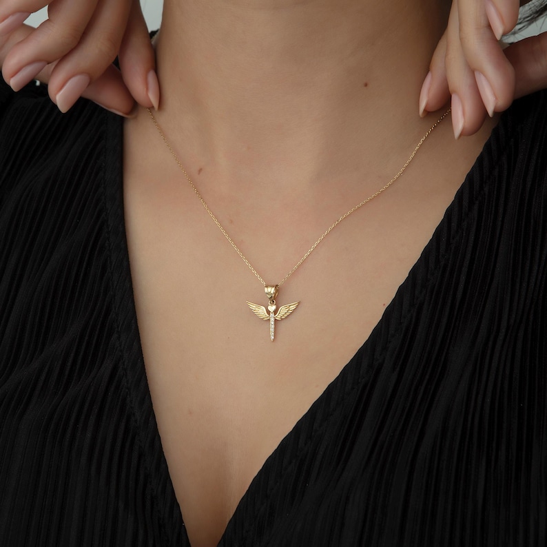 May include: A gold necklace with a pendant featuring a stylized angel with wings and a heart in the center.