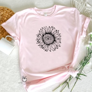 Puede incluir: Una camiseta rosa con un dibujo de l&iacute;nea negra de un girasol en la parte delantera. La camiseta est&aacute; hecha de un material suave y c&oacute;modo y tiene un cuello redondo.