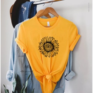 Puede incluir: Una camiseta amarilla con un gr&aacute;fico de girasol negro. La camiseta est&aacute; anudada a la cintura.