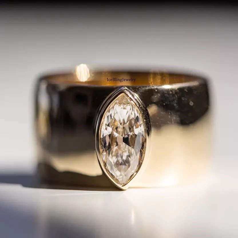 Einzigartig dieser mutige Ring hat 1 CT Marquise-Schnitt Simulierte Diamant-Lünette in einem klobigen Zigarrenband für ein modernes Gefühl, das wundervoll aussieht