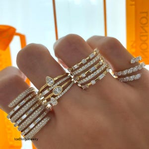 Può includere: Una collezione di anelli d'oro con vari design, tra cui fasce con piccoli diamanti, pietre taglio baguette e gemme a forma di pera. Gli anelli sono esposti su una mano, mostrando i loro diversi stili e la loro brillantezza.