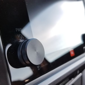 May include: Close-up of a black volume knob with a silver centre, labelled "PWR" and "VOL" on a car dashboard.
