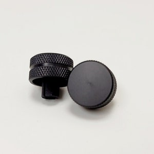 May include: Two black knobs with a textured surface. One knob has a smooth top and the other has a ridged top.