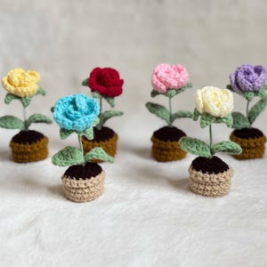 May include: Six crocheted flower pots with different coloured flowers. The flowers are yellow, red, blue, pink, white and purple. The pots are brown and beige.