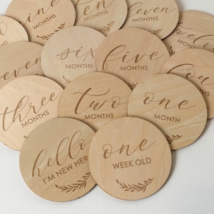 Pu&ograve; includere: Una collezione di segnapunti circolari in legno. Ogni disco &egrave; inciso con un mese o una frase come "hello I'm new here" e "one week old" in elegante scrittura. Il tono naturale del legno e il design semplice creano un'estetica affascinante.