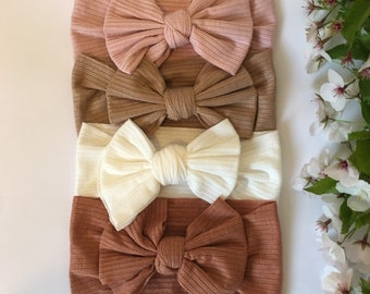 Può includere: Quattro fasce per capelli a costine di diversi colori con fiocchi. Le fasce sono in tonalità rosa, marrone, bianco e arancione.
