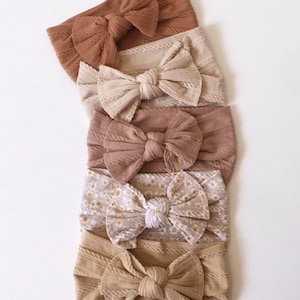 May include: Five different hair scrunchies with a knotted bow design. The scrunchies are in shades of brown, beige, and white. One scrunchie has a floral pattern.