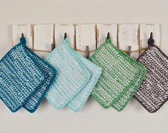 May include: Five crocheted pot holders hanging on a white wooden rack. The pot holders are in shades of blue, green, and gray.
