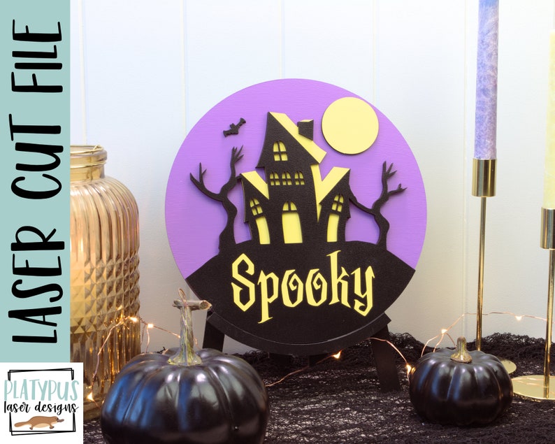 May include: Purple and black Halloween-themed round sign with a silhouette of a spooky house and the word "Spooky" in yellow letters.