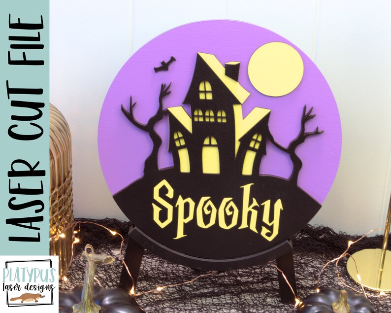 May include: Purple and black Halloween sign with a spooky house and a full moon. The sign says "Spooky" in a black font.