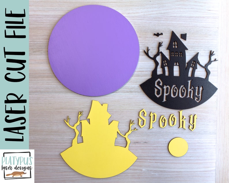 May include: A laser cut file for a spooky Halloween themed craft project. The file includes a purple circle, a black silhouette of a haunted house with the word "Spooky" underneath, a yellow silhouette of a haunted house, and the word "Spooky" in a decorative font.