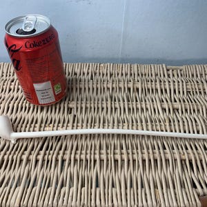 Puede incluir: Pipa de fumar de cerámica blanca con una punta roja, descansando sobre una superficie de mimbre. Una lata de Coca-Cola Zero es visible en el fondo.