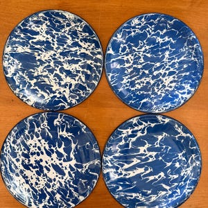 May include: A set of four round plates featuring a marbled pattern of deep blue and white swirls. Each plate has a smooth, glossy finish with a consistent color distribution across the surface, creating a distinct wave-like appearance on every piece.