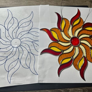 May include: A stained glass sunburst design with red, orange, and yellow glass pieces. The design is numbered with a pattern for creating the stained glass piece.
