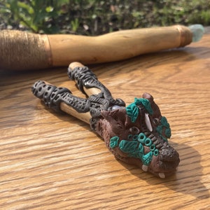 May include: A brown and black clay dragon head with green leaves and white teeth. The dragon head is sitting on a wooden surface.