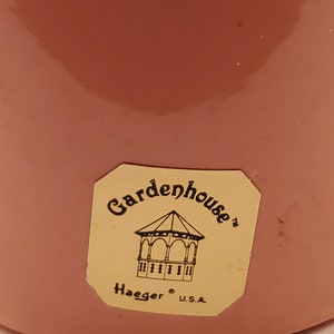 May include: A pink ceramic planter with a yellow sticker that says "Gardenhouse" with a small illustration of a gazebo and the text "Haeger U.S.A."