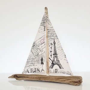 Könnte beinhalten: Ein kleines Segelboot aus Treibholz mit einem weißen Segel, das mit einem schwarz-weißen Eiffel-Turm-Design und dem Wort "PARIS" verziert ist.
