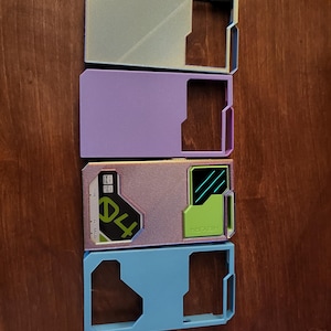 May include: Four rectangular card holders in pastel colors: light green, purple, pink, and blue. The pink holder has the number "04" and the word "REVURA" printed on it. Each holder has a cutout section on one side.