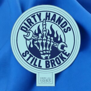 May include: A light blue sticker with the text "DIRTY HANDS STILL BROKE" in a circular design. The design features a skeleton hand giving the middle finger, holding a wrench, and flames. The sticker has a small rectangular tab at the bottom with the letters "BLC".
