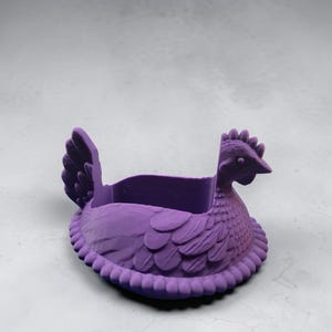 Puede incluir: Una maceta morada con forma de gallina. La maceta est&aacute; dise&ntilde;ada con un patr&oacute;n de plumas detallado y un borde con cuentas. La gallina tiene una cresta y un pico detallados. La maceta est&aacute; hecha de un material s&oacute;lido y es adecuada para plantas peque&ntilde;as o art&iacute;culos decorativos.