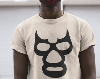 May include: A person wearing a beige t-shirt with a black wrestling mask graphic. The person is wearing a black baseball cap and has a red beard.