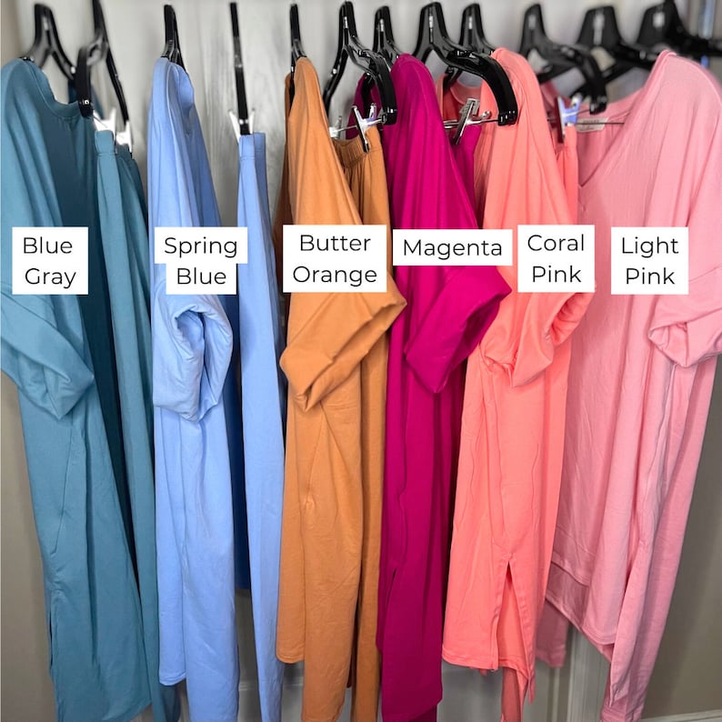 Op de afbeelding: Zeven verschillende gekleurde T-shirts hangen aan hangers. De kleuren zijn blauwgrijs, lenteblauw, botergeel, magenta, koraalroze en lichtroze.