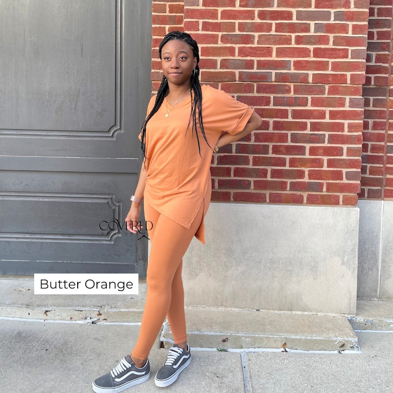 Op de afbeelding: Een tweedelige outfit in een botergele kleur. De outfit bestaat uit een shirt met korte mouwen en een V-hals en een legging. Het model draagt de outfit en staat voor een bakstenen muur.
