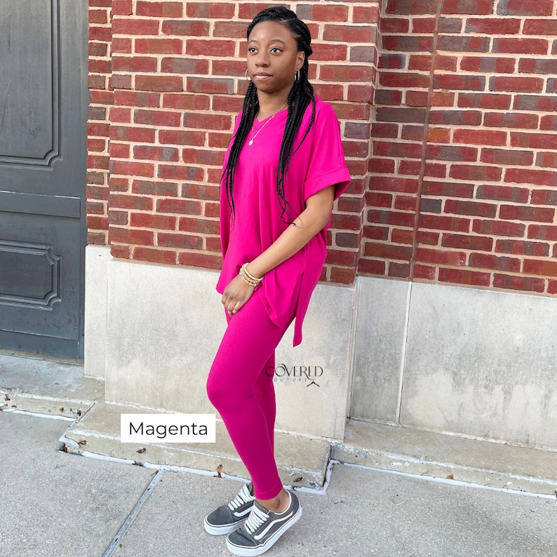 Op de afbeelding: Een magentakleurige twee-delige outfit met een lang mouwloos topje en leggings. Het topje heeft een losse pasvorm en een licht afgeronde halslijn. De leggings zijn strak en hebben een rechte pijp. Het model draagt zwarte sneakers.