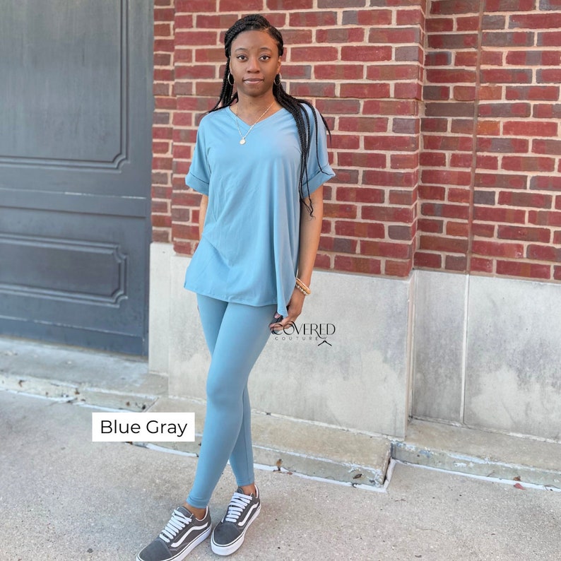 Op de afbeelding: Een blauwgrijze twee-delige outfit met een top met korte mouwen en een v-hals en leggings. De outfit is gemaakt van een zachte, comfortabele stof en is perfect voor casual wear. "Covered Couture" is gedrukt op het rechterbeen van de leggings.