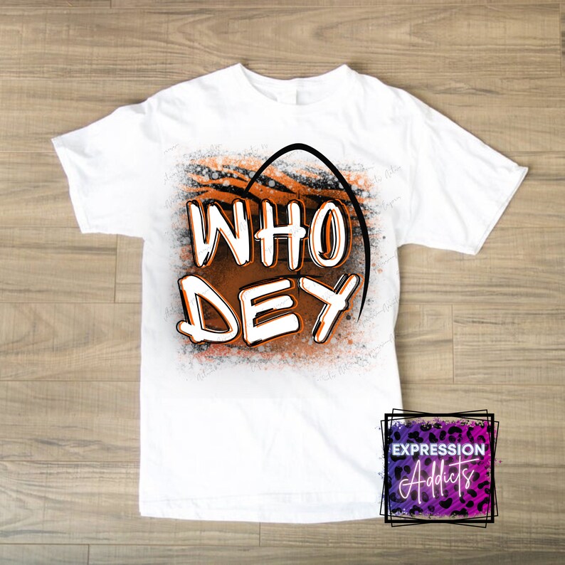 Puede incluir: Camiseta blanca con el texto "WHO DEY" en letras naranjas y blancas, sobre un dise&ntilde;o de rayas de tigre. La camiseta tiene cuello redondo y mangas cortas. El logotipo de Expression Addicts est&aacute; en la esquina inferior derecha.