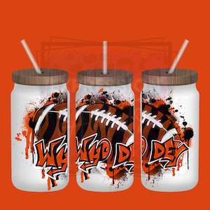 May include: Three white glass tumblers with wooden lids and straws. Each tumbler features a football design with orange and black stripes and the words "Who Dey" in graffiti style. The background is orange.