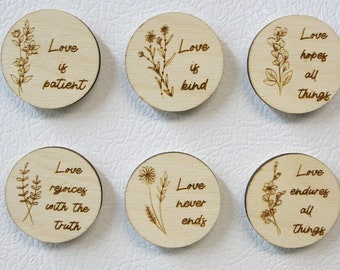 May include: Six round wooden magnets with laser-etched floral designs and inspirational quotes about love. The quotes include "Love is patient," "Love is kind," and "Love hopes all things."