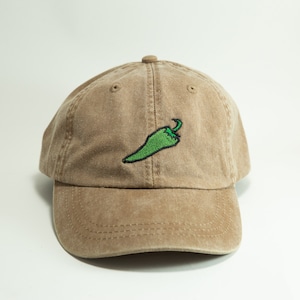 May include: A brown baseball cap with a green chilli pepper embroidered on the front.