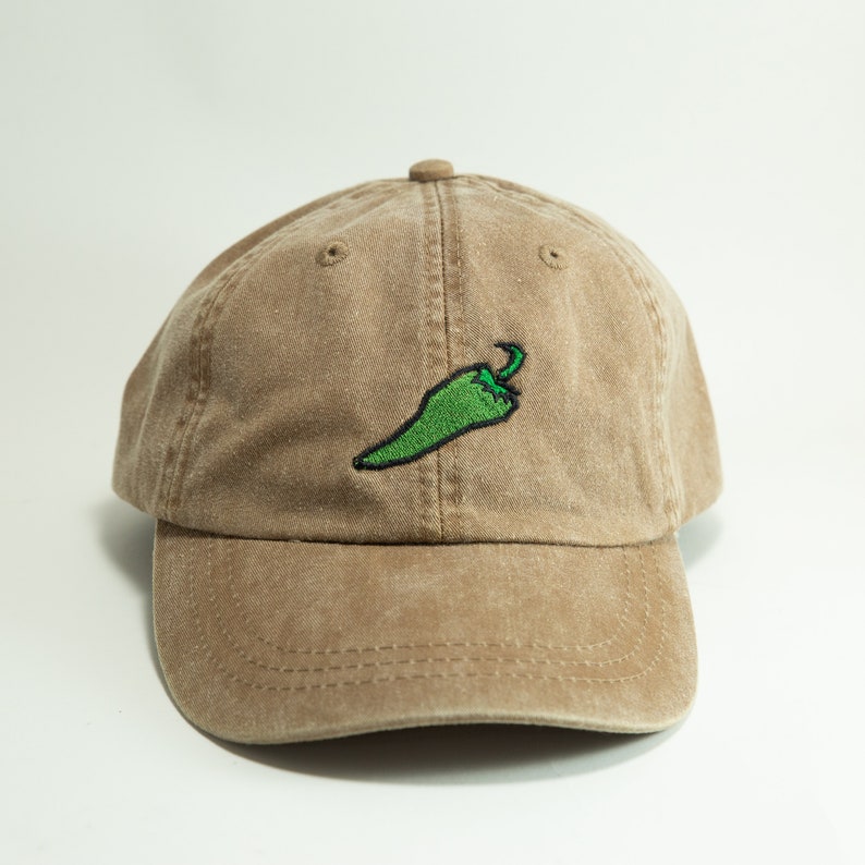 May include: A brown baseball cap with a green chilli pepper embroidered on the front.