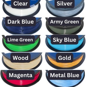 May include: A collection of ten circular spools of 3D printer filament in various colors, each labeled with its corresponding color name: Clear, Silver, Dark Blue, Army Green, Lime Green, Sky Blue, Wood, Gold, Magenta, and Metal Blue.